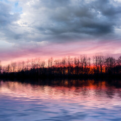 Obraz premium dramatic sunset over the forest silhouette reflected in a lake