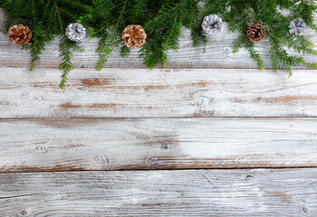 Top border of silver and gold color pine cone ornaments with real fir branches on white rustic wood...
