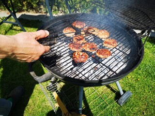 Barbecue grill. Hand preparing meatballs on barbecue kettle in backyard.