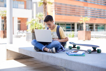 Caucasian boy high school student using laptop computer outdoors. Space for text.