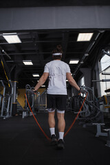Fototapeta na wymiar Vertical rear view shot of a male athlete exercising, jumping with skipping rope