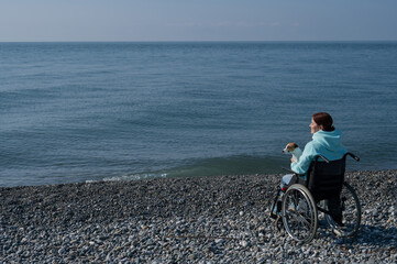 Caucasian woman in a wheelchair cuddling with a dog near the sea. 