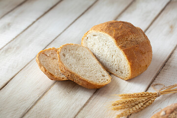Fresh baked sliced loaf of bread with wheat on wooden background