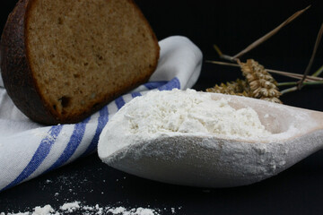 Close-up/Nahaufnahme von Brot mit Handtuch, Getreide und Mehl vor schwarzem Hintergrund