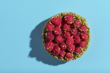 Top view on raspberry tartlet with pistachios on a blue background