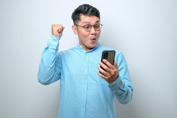 Shocked young good looking Asian man using smartphone to read good news online