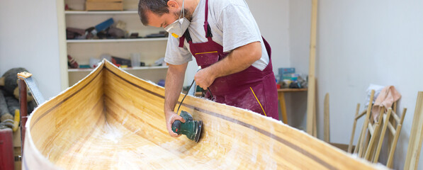 Young carpenter making wooden boat in his carpentry workshop - 517379183