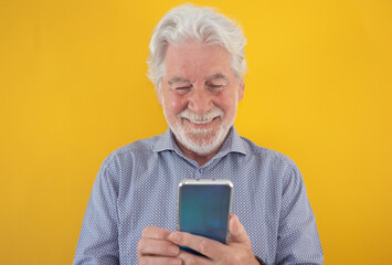 Portrait of beautiful senior man isolated on yellow background while using phone reading a message