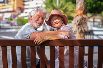 Portrait of beautiful senior caucasian couple sitting on a bench looking at camera - happy retired people enjoying free time