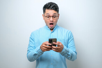 Shocked young good looking Asian man using smartphone to read good news online isolated