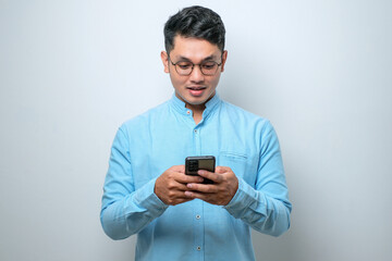 Smiling young good looking Asian man using smartphone to get in touch with family and friends...