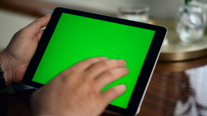 Adult hand swiping green tablet screen closeup. Man holding chroma key computer