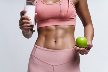 Woman showing her six pack while holding green apple and glass of milk for stay healthy .