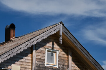 The concept of travel in Russia. Corner of roof of old wooden house with patterns on edges against blue sky. One of most beautiful villages of Karelia Kinerma in summer.