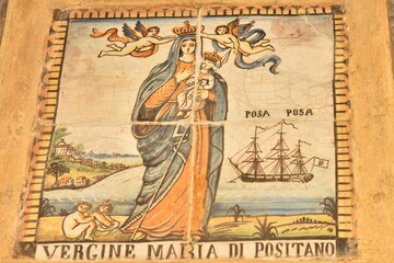 Fototapeta na wymiar Riggiole tile mural depicting the patron saint of local sailors and fishermen, the Virgin of Positano holding baby Jesus, Amalfi coast motives and an old sailing ship in the back, Positano, Italy