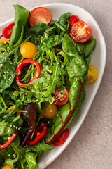 Salad of fresh farm vegetables in an oval dish on a pink background, sitya lettuce and chard, tomatoes and colorful bell peppers, arugula and sesame seeds