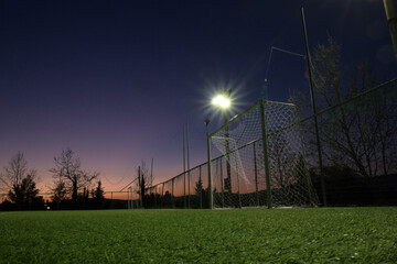Photo shows a football field with soccer goals with the lights on. Low angle view .