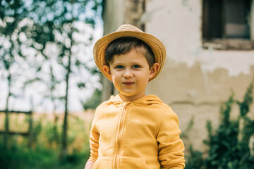Little boy in hat and yellow jacket plays in a garden