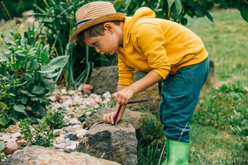Little boy in hat and yellow jacket plays in a garden