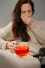 Mug of hot tea for colds and flu is holding a woman suffering from a viral infection. Concept of seasonal illness.