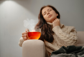 Woman sitting at home on the sofa unhealthy with a cup of hot tea. Fever and seasonal flu concept.