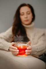 Woman warms her hands on a glass mug of tea after a winter walk.