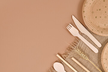 Eco friendly paper party plates and wooden cutlery in corner of beige background with copy space