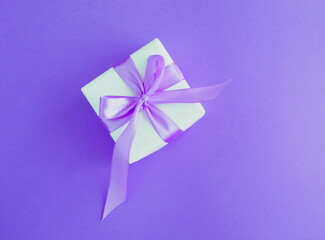 Closeup on gift box with tied purple bow on the purple background. Top view.
