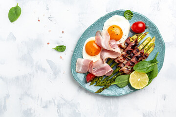 Fototapeta na wymiar Ketogenic diet. Keto brunch breakfast. fried eggs, asparagus wrapped in bacon, ham, tomatoes and salad. Long banner format. top view
