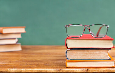 glasses on a stack of books standing on a wooden table against the background of a blackboard