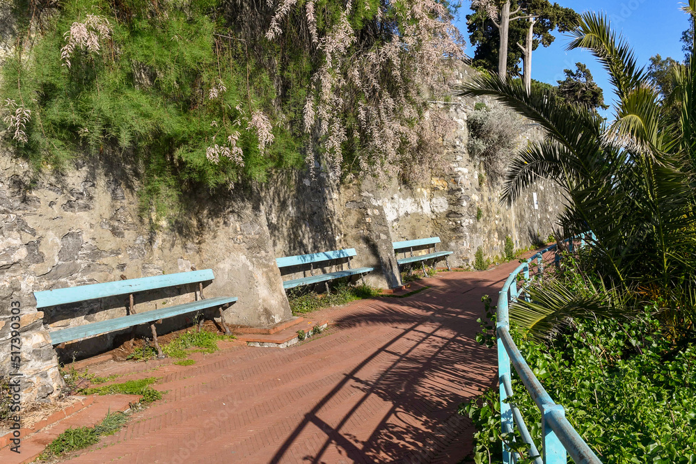 Wall mural A stretch of the Anita Garibaldi Promenade, popular tourist attraction of the fishing village, with blue benches against an old stone wall in springtime, Nervi, Genoa, Liguria, Italy