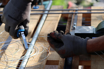 Man holds pliers and steel wire. Handyman tools close up photo. Male hands in grey protective gloves. 