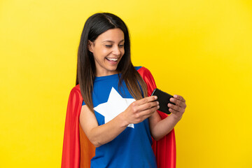 Super Hero woman isolated on yellow background playing with the mobile phone