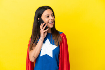 Super Hero woman isolated on yellow background keeping a conversation with the mobile phone with someone