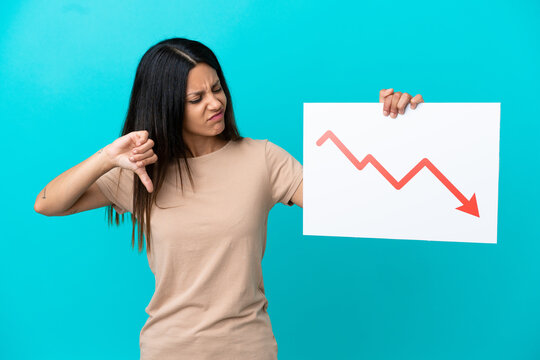 Young woman over isolated background holding a sign with a decreasing statistics arrow symbol and doing bad signal