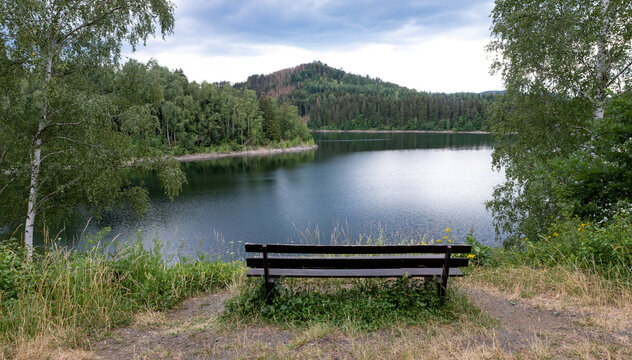 Wooden bench on a hill, against the backdrop of a picturesque landscape, a lake, mountains and a forest.