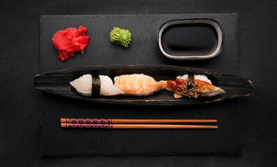 Elegant sushi set composition with fresh shrimp and raw salmon served with ginger, wasabi and soy sauce shooting from above. Traditional japanese meal on black table with wooden chopstick