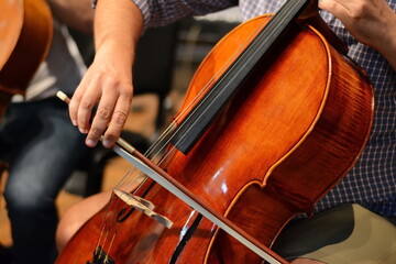 Symphony orchestra on stage, hands playing cello. Professional cello player's hands close up, he is...