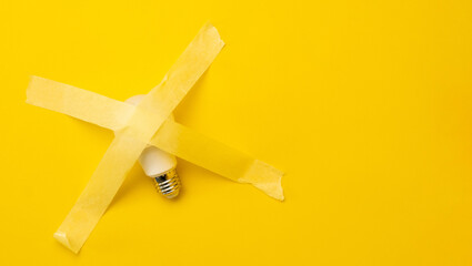 Lamp sticked up with masking tape isolated in yellow background with copy space. Concept of society with no ideas, creativity and thoughts. Forbidden solution