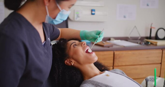 Dentist with face mask checking teeth of female patient with mirror tool during dental appointment. African woman having routine checkup to prevent tooth decay and gum disease with good oral hygiene