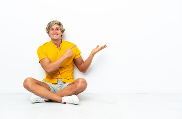 Fototapeta premium Young English man sitting on the floor holding copyspace imaginary on the palm to insert an ad