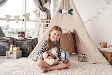 Little girl with teddy bear and globe sitting in wigwam settled in playroom © Ievgen Skrypko