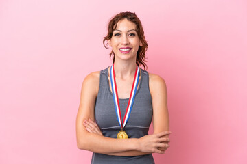 Young caucasian woman with medals isolated on pink background keeping the arms crossed in frontal...