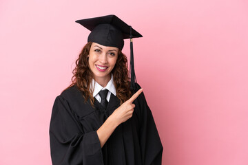 Young university graduate woman isolated on pink background pointing to the side to present a product