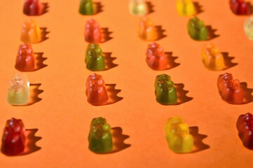 Assortment of colored gummy bears on an orange background and with the reflection to their side of the hard light passing through them