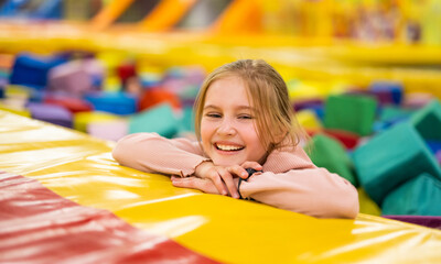 Fototapeta na wymiar Pretty girl kid sitting in colorful cube trampoline at playground park and smiling. Beautiful female child happy during active entertaiments indoor