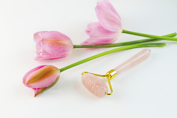 Rose quartz roller for the face next to the flowers of pink tulips. High quality photo
