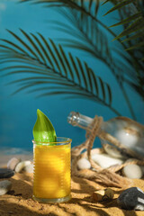 Tropical concept. Drinks. Mango smoothie in a glass on the ocean with a palm tree and a bottle, rope. Bright sunlight, beach, golden sand, sea stones. Background image, copy space