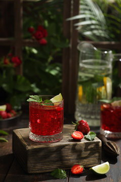 Summer soft drinks. Mojito with strawberries, lime, ice and mint in a glass. A pitcher of lemonade in the summer kitchen in garden. Green trees, sunlight. Rustic. Background image, copy space