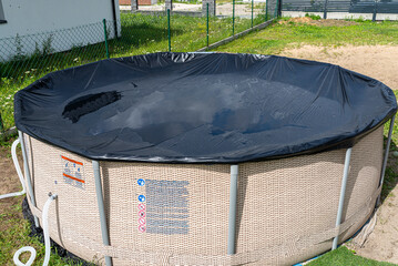 Large expansion pool with a diameter of 3.96 meters with black cover, set in the backyard next to...
